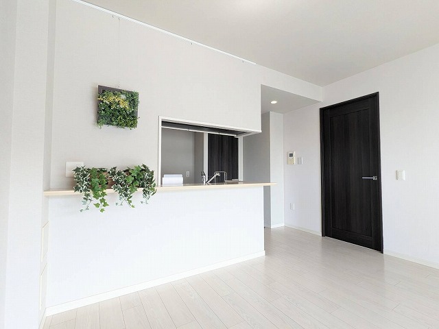 床は白いフローリングで壁はライトグレーのクロスです。対面式キッチンです。アクセントで壁にグリーンを飾っています。