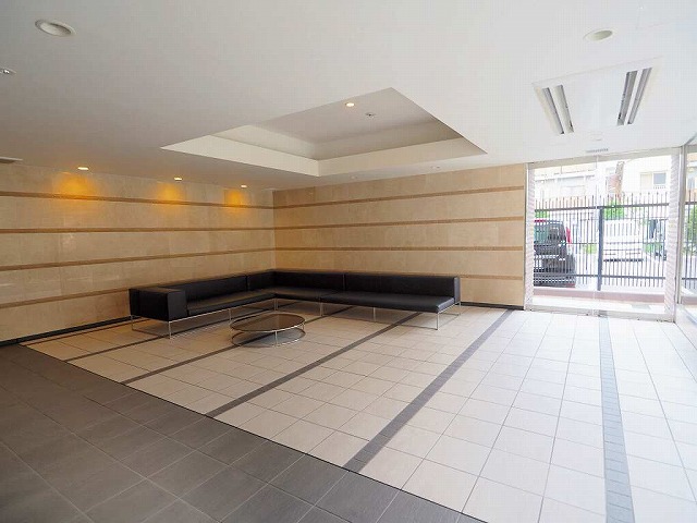 ライオンズ志村ローレルコートのエントランスホールです。床はタイルです。広い空間に高級感のある黒いL字型ソファと丸いテーブルが置いてあります。