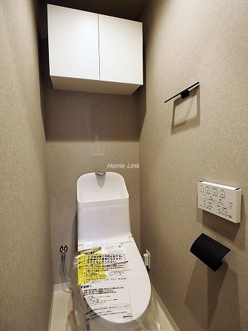 トイレは温水洗浄機能付きです。上部に扉付き収納があります。壁はベージュです。